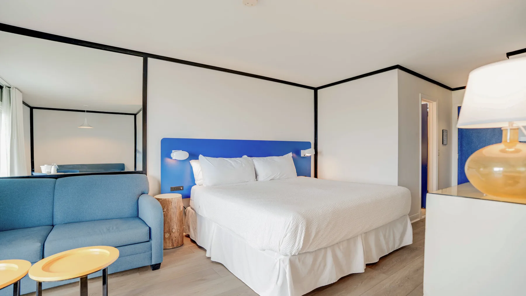 Un dormitorio con una cama blanca, asientos azules y una mesita.