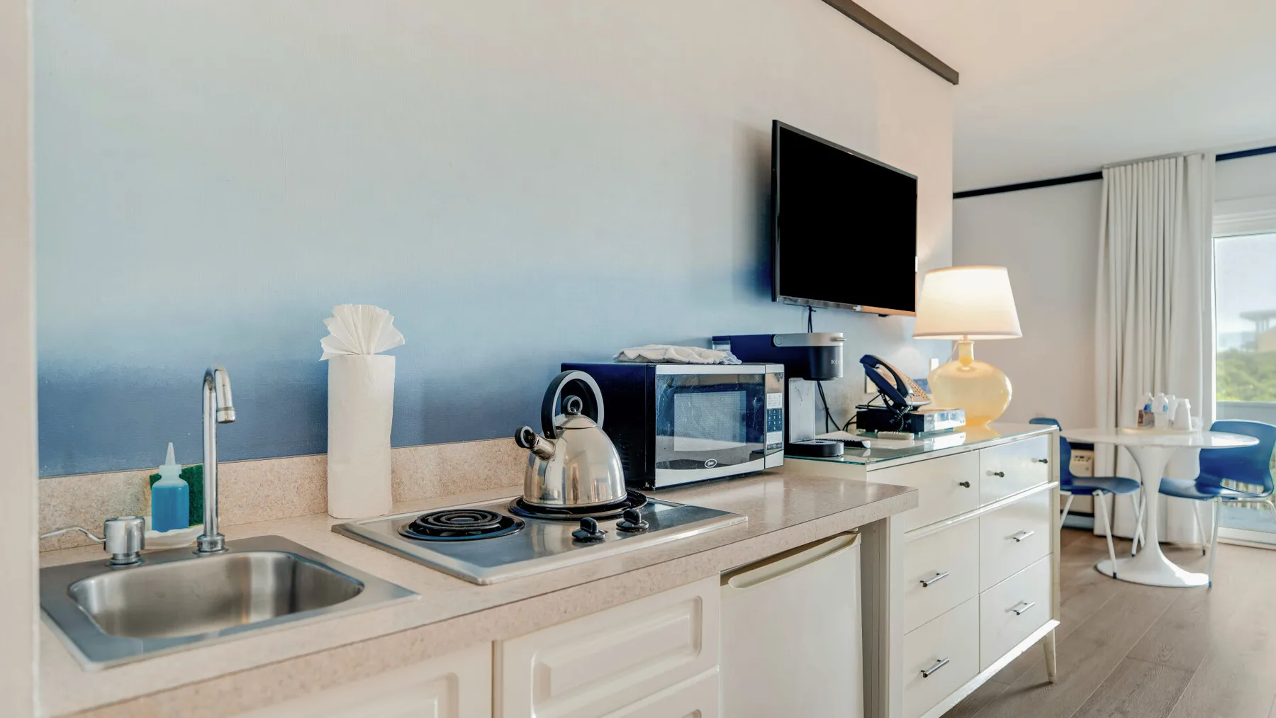 Una pequeña cocina con fregadero y estufa queda bajo un televisor montado en la pared.