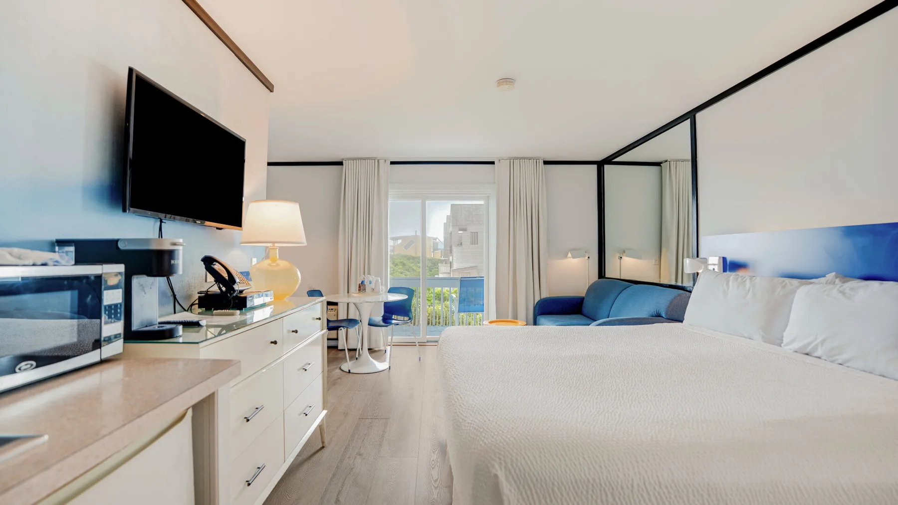 Un dormitorio luminoso con una cama grande, un televisor y puertas de vidrio que dan a un balcón.