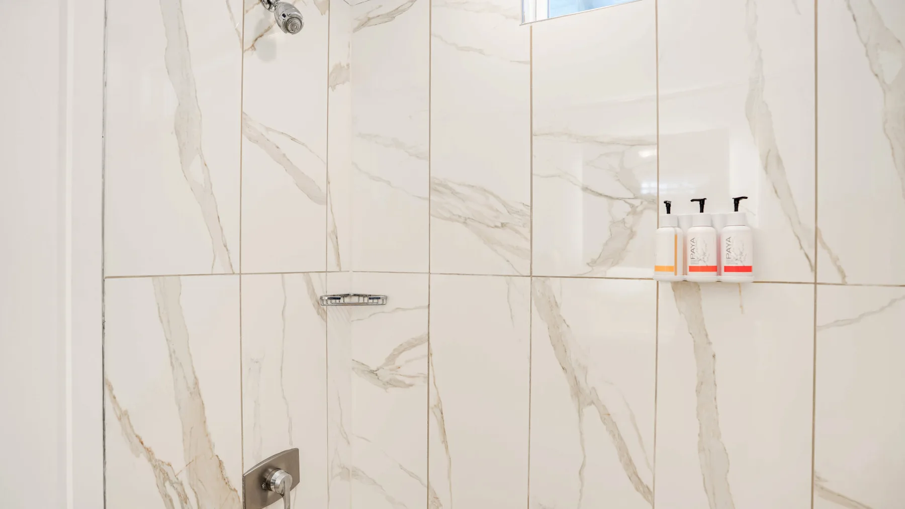 Una zona de ducha con azulejos, controles en la pared y dispensadores de artículos de aseo.