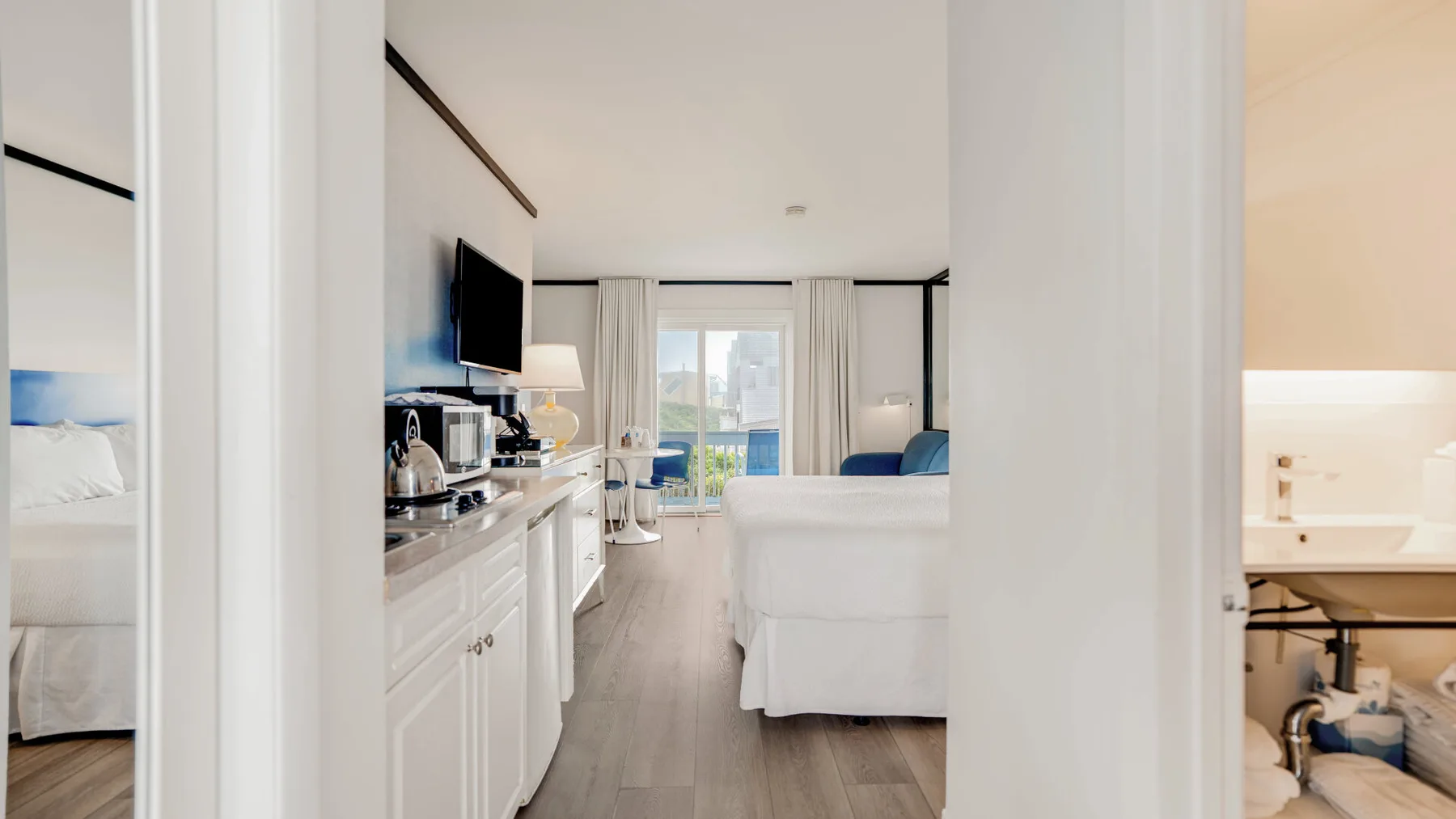 Un dormitorio luminoso se abre a una zona de estar con televisor y ventanales.