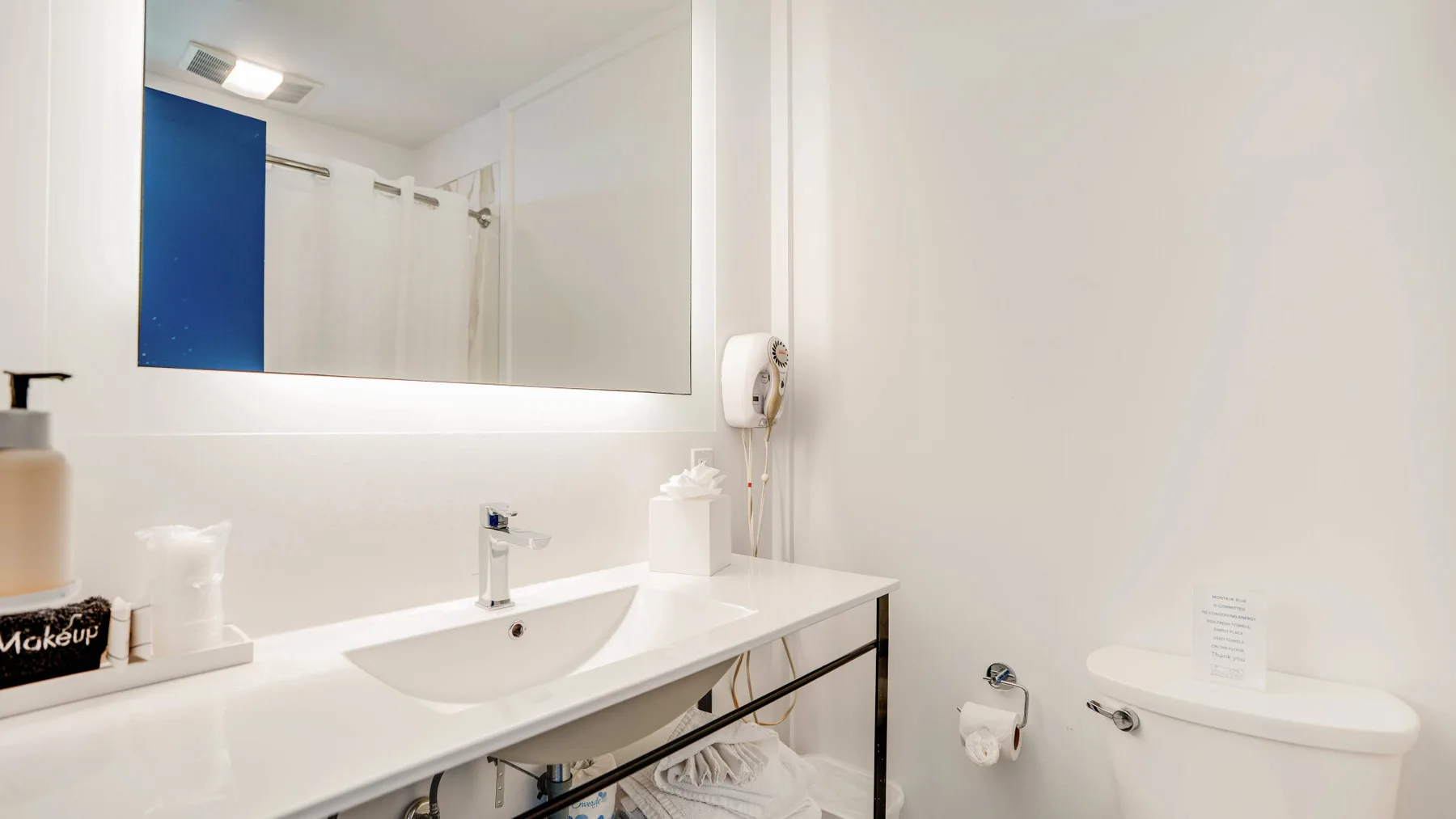 Un baño luminoso con un espejo amplio sobre un lavabo y una encimera blancos.