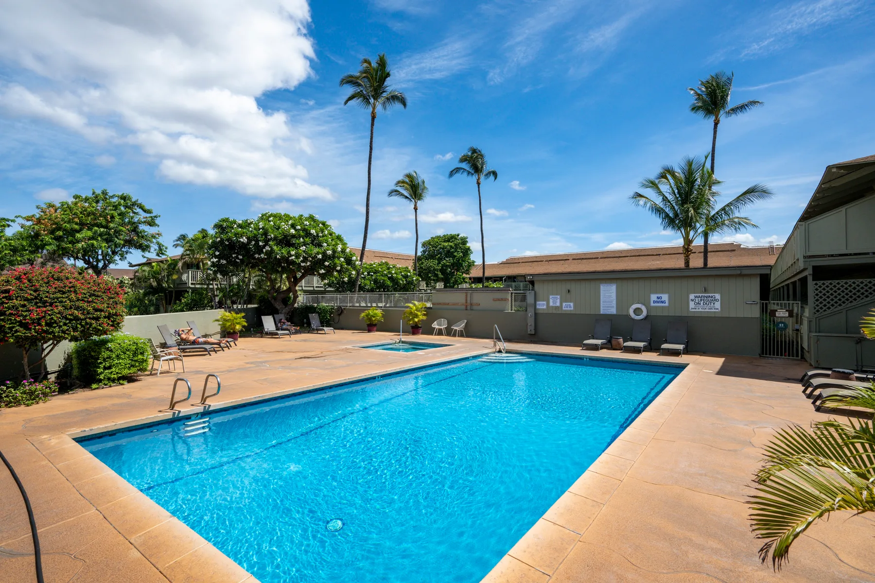 Una piscina al aire libre está rodeada por una terraza soleada y vegetación tropical.