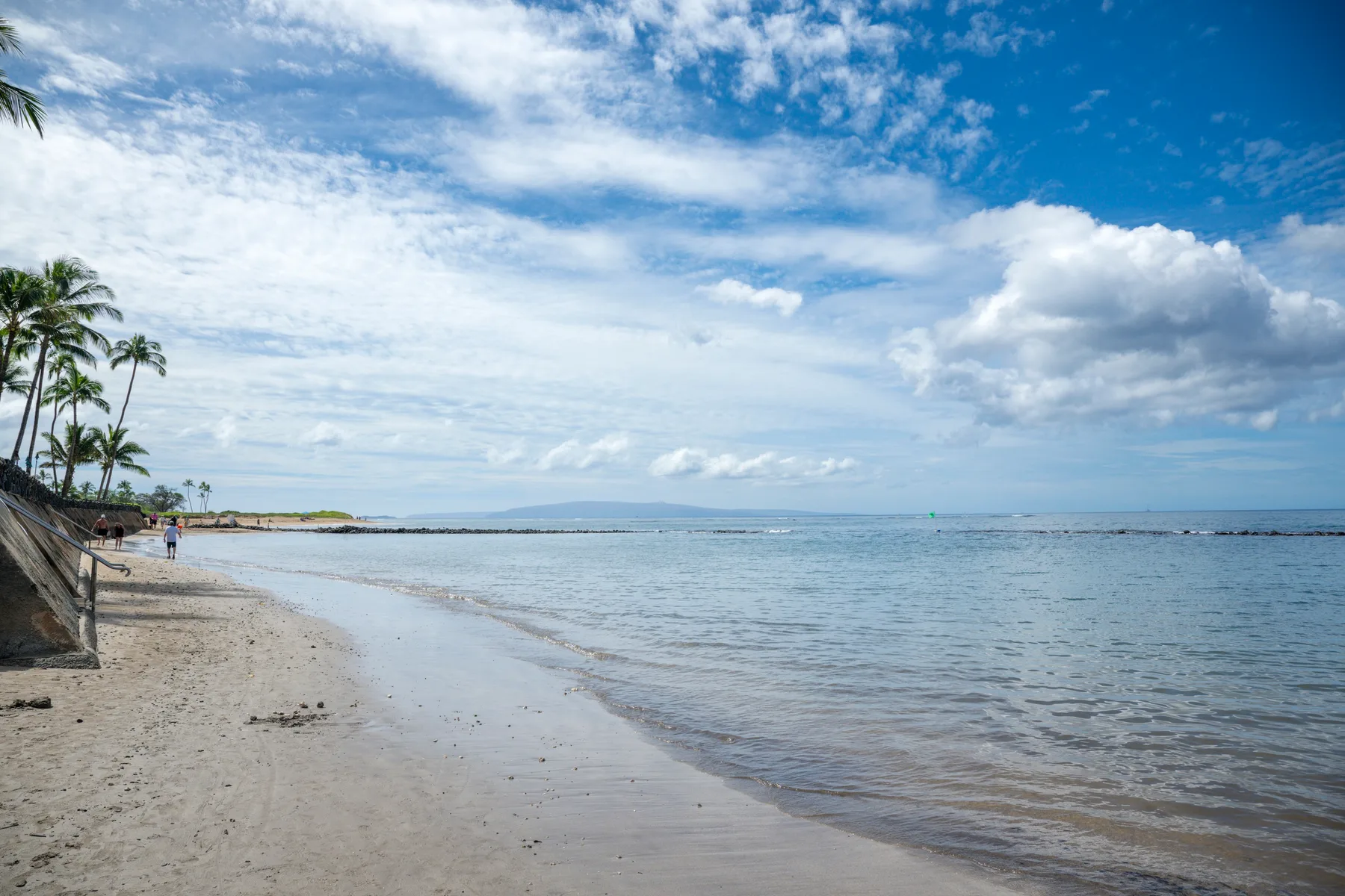Una playa de arena bordea aguas tranquilas bajo un cielo parcialmente nublado.