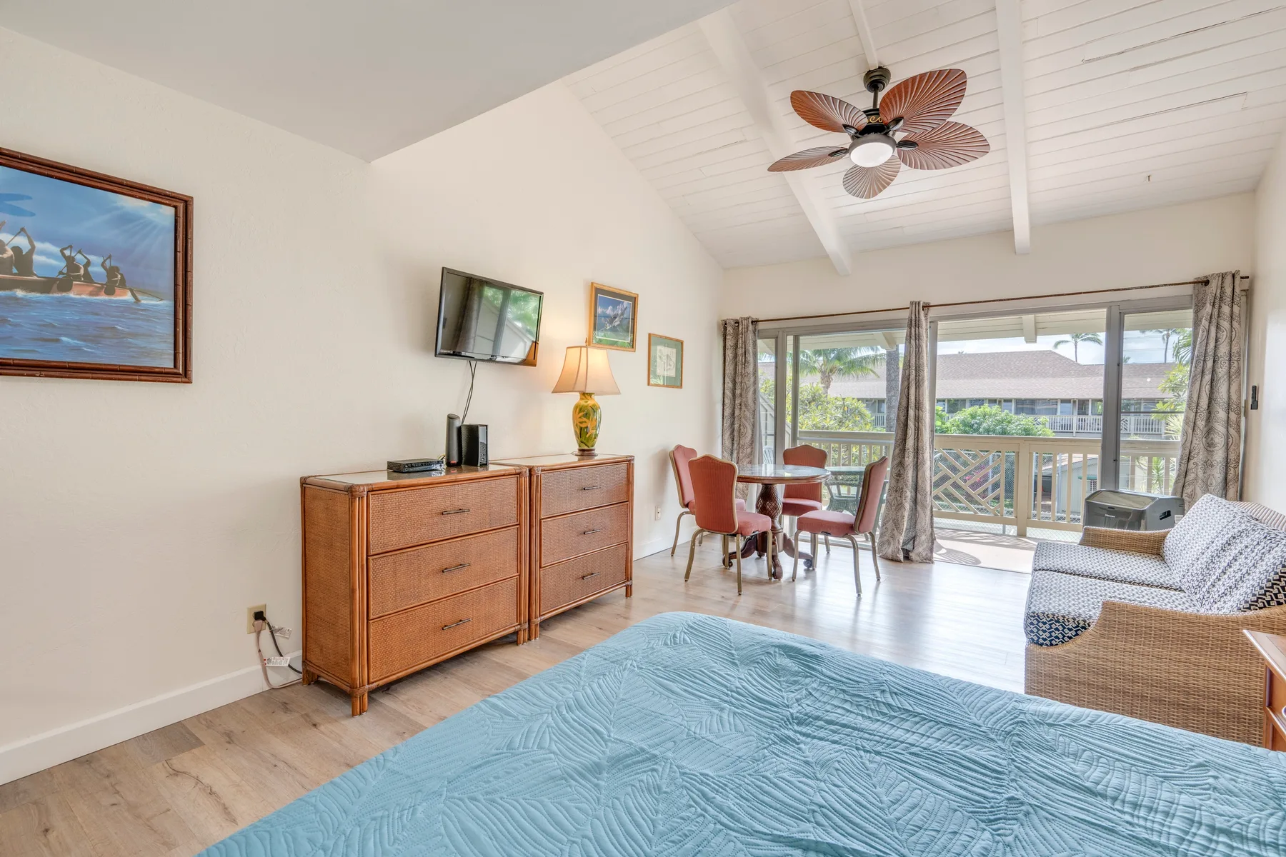 Un dormitorio con una cómoda de madera, una zona para sentarse y puertas corredizas de vidrio hacia un balcón.