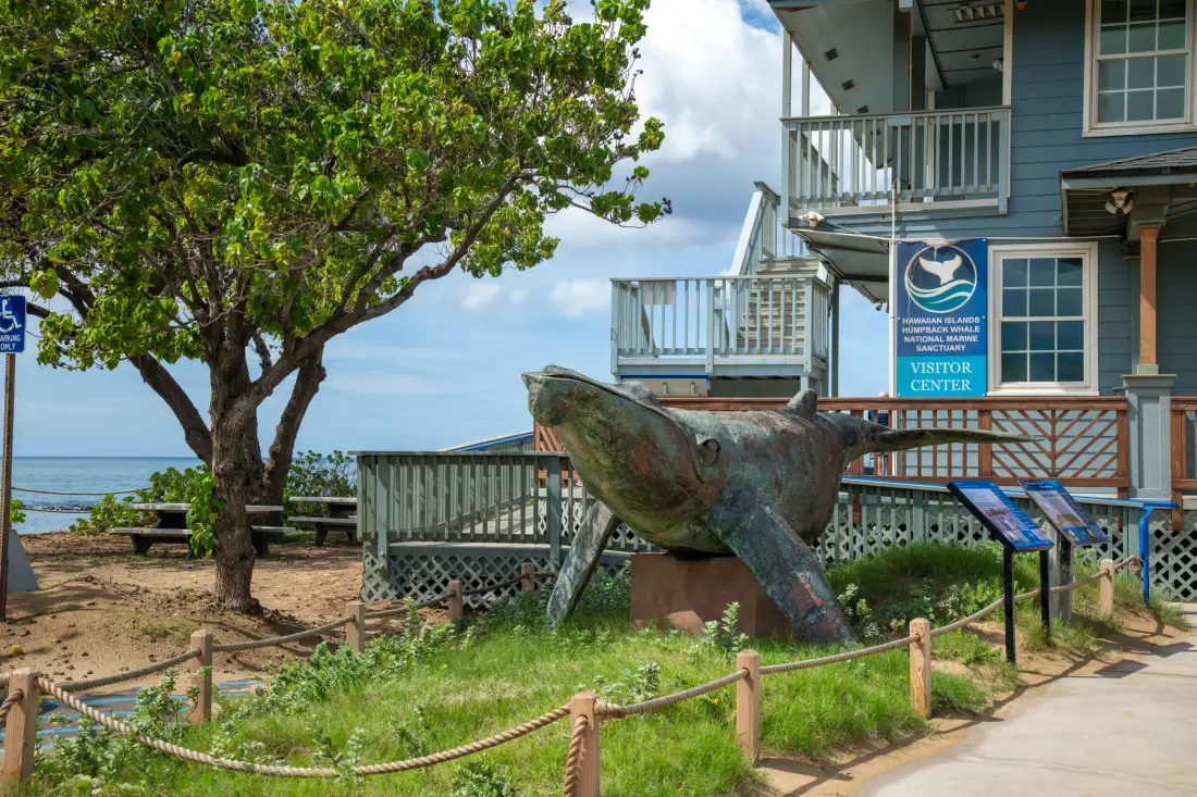 Una gran escultura de ballena está junto a un centro de visitantes cerca del agua.