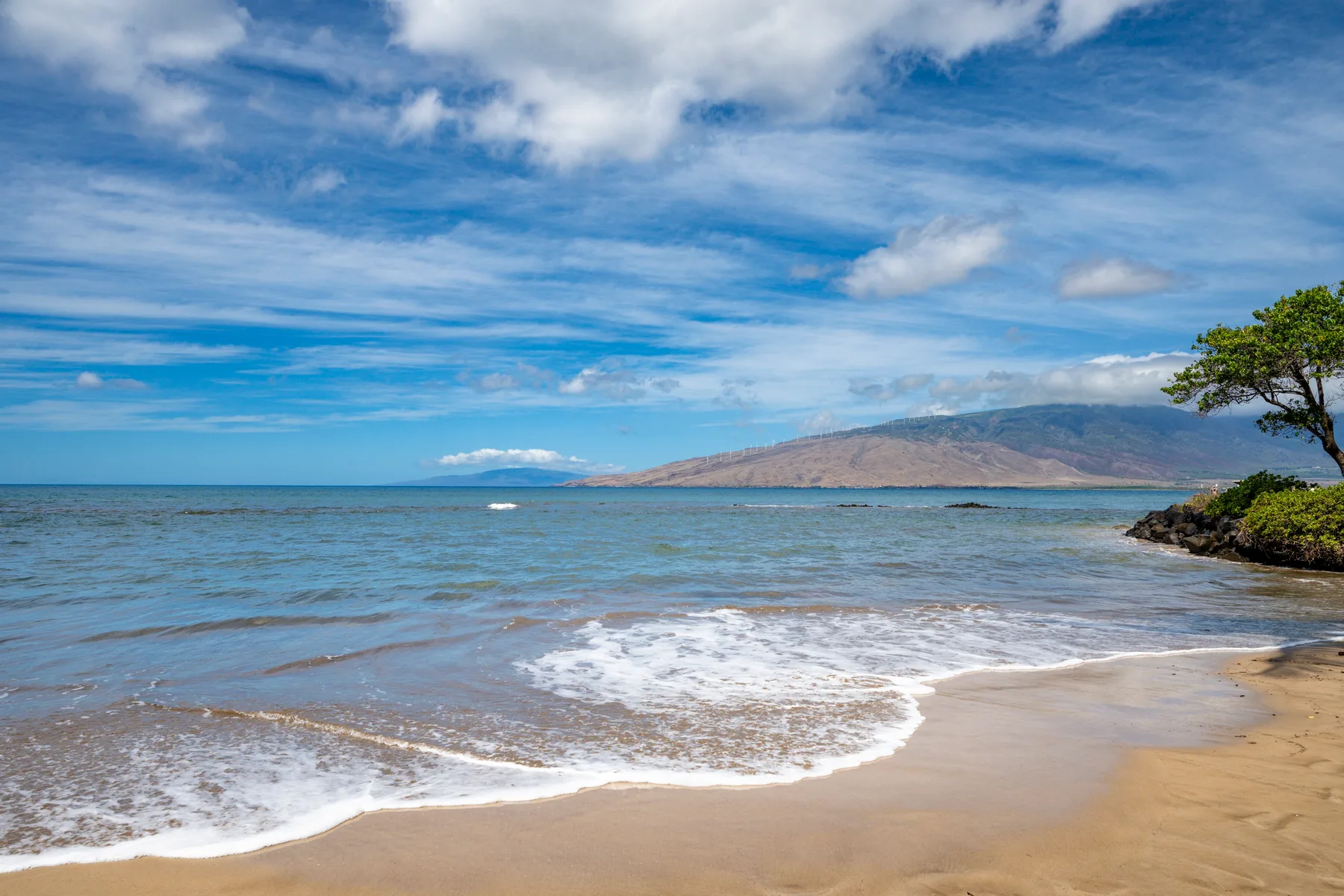 Una playa de arena se encuentra con el océano bajo un cielo azul y nublado.