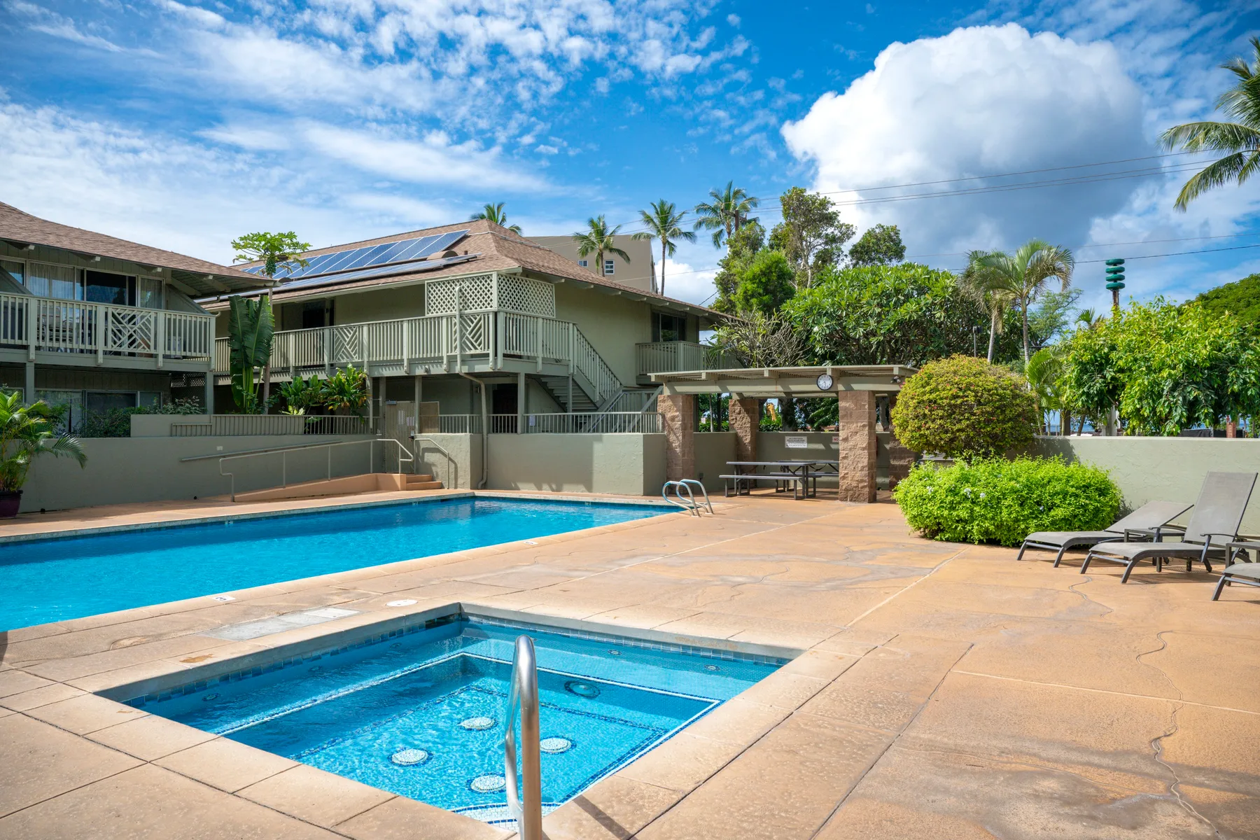 Una piscina y un jacuzzi al aire libre están junto a un patio soleado con asientos.