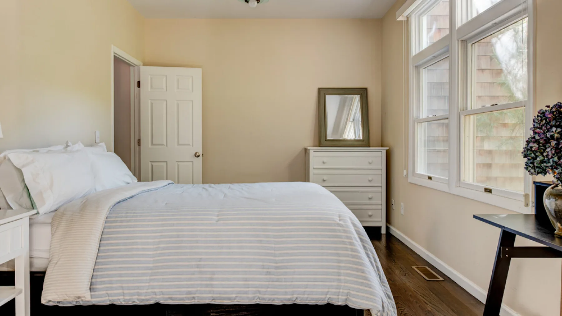 A bedroom with a neatly made bed beside large windows.