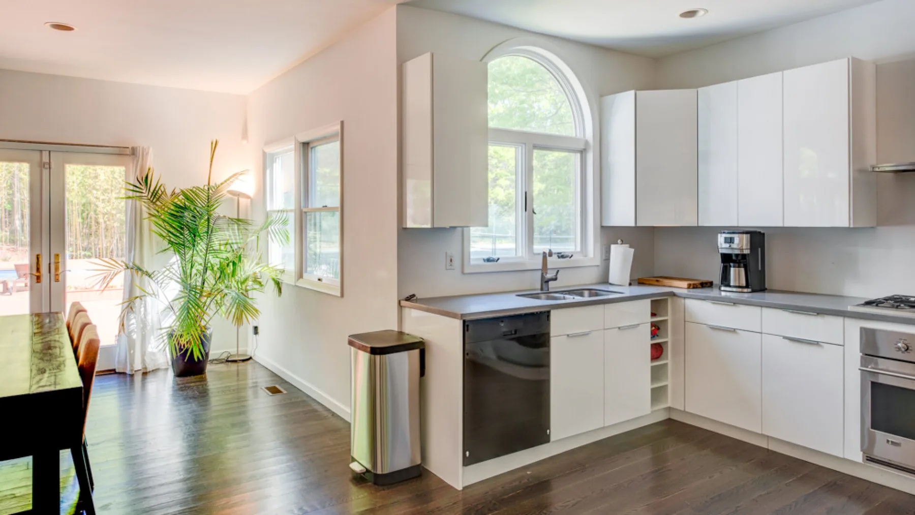 A bright kitchen opens into a dining area, with white cabinets and a large window.