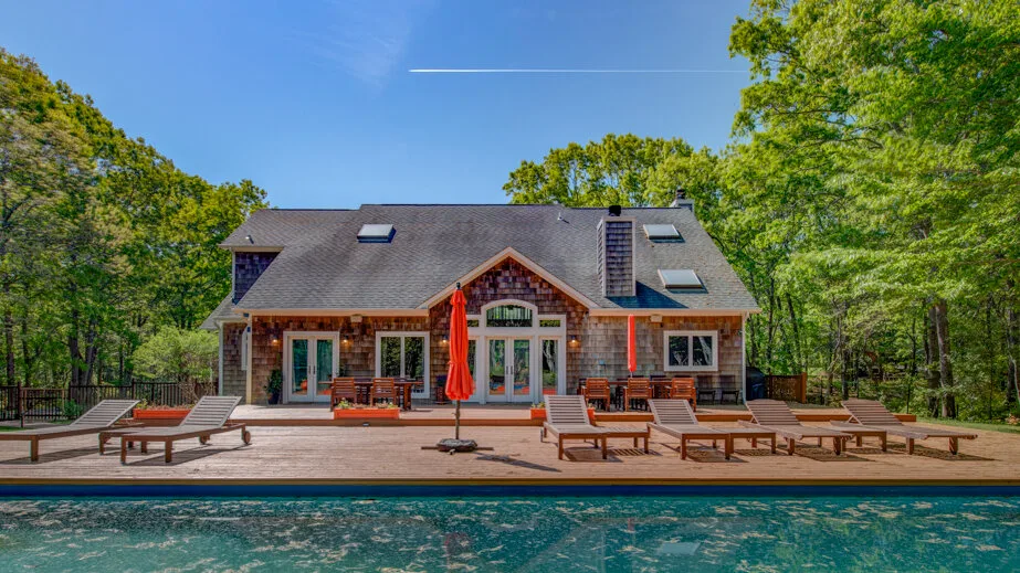 A large house overlooks an outdoor swimming pool and wooden deck.