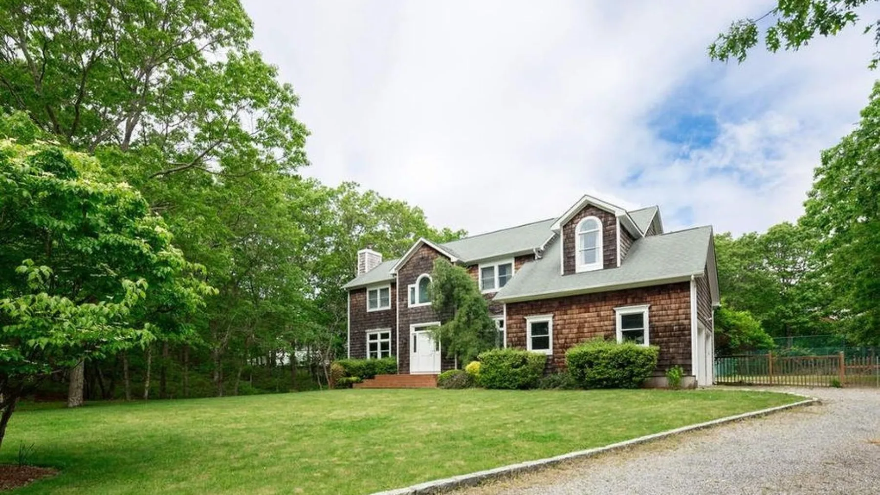 A large house stands beside a broad lawn, with trees around the property.