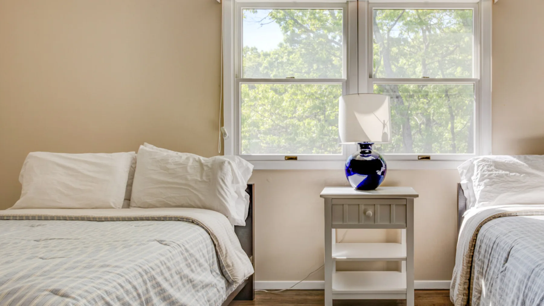 A bright bedroom with two beds beside a large window.