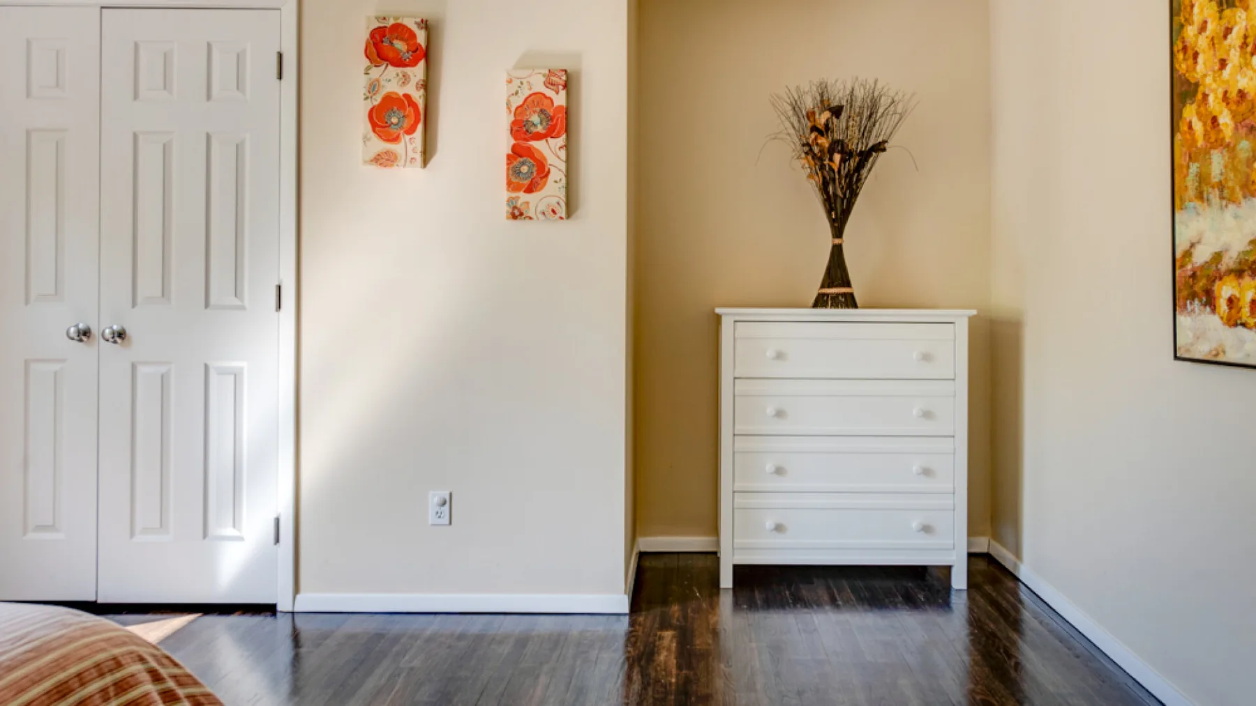 A bedroom with a white dresser, decorative artwork, and dark flooring.