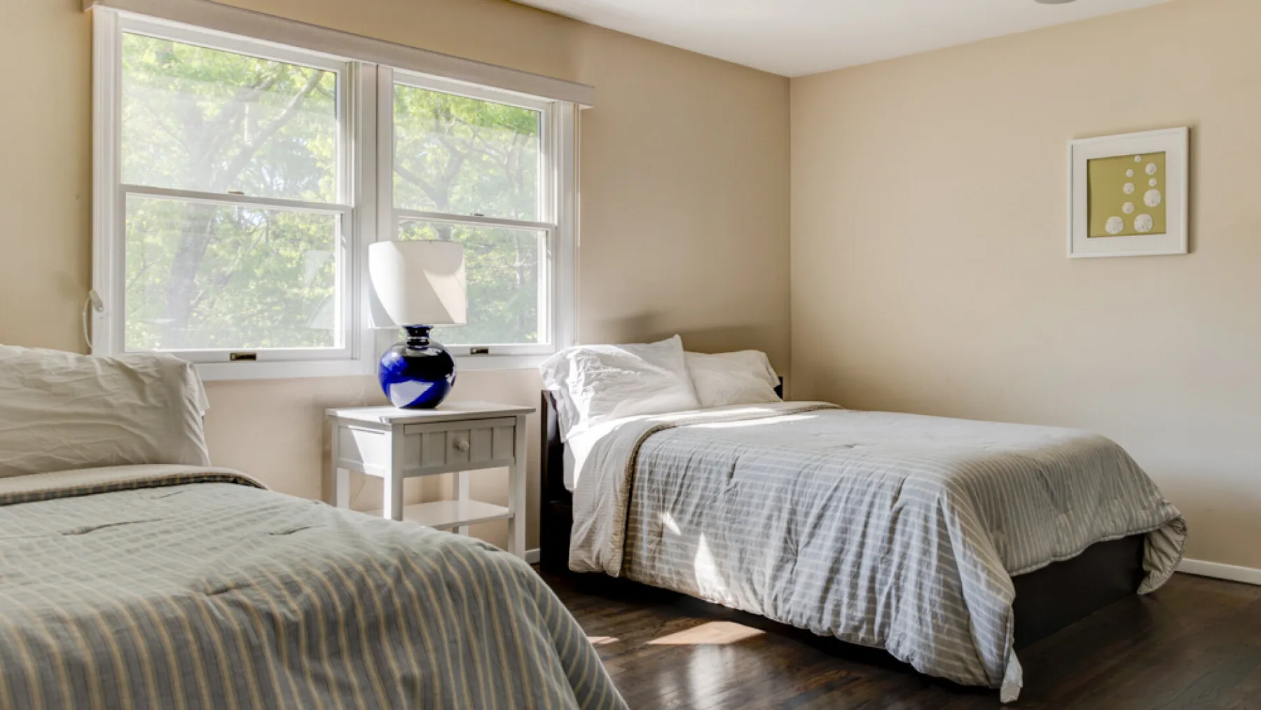 A bright bedroom with two beds beside large windows.