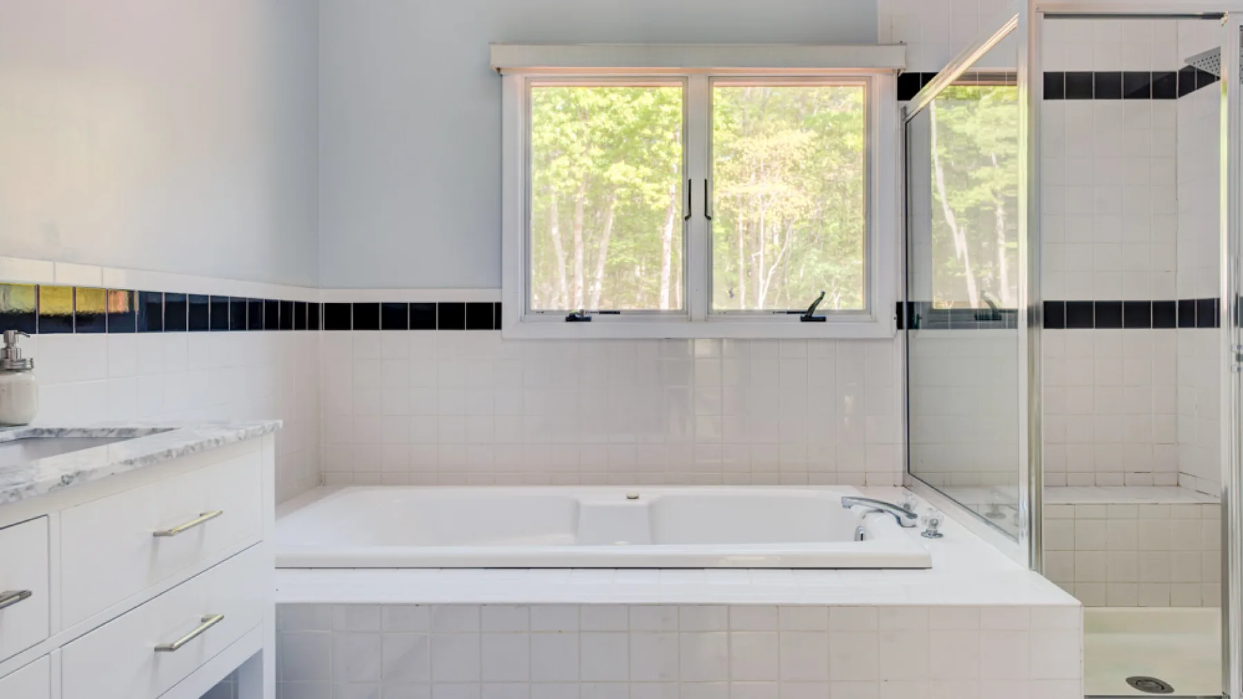 A bright bathroom with a bathtub beneath a window and a glass shower.