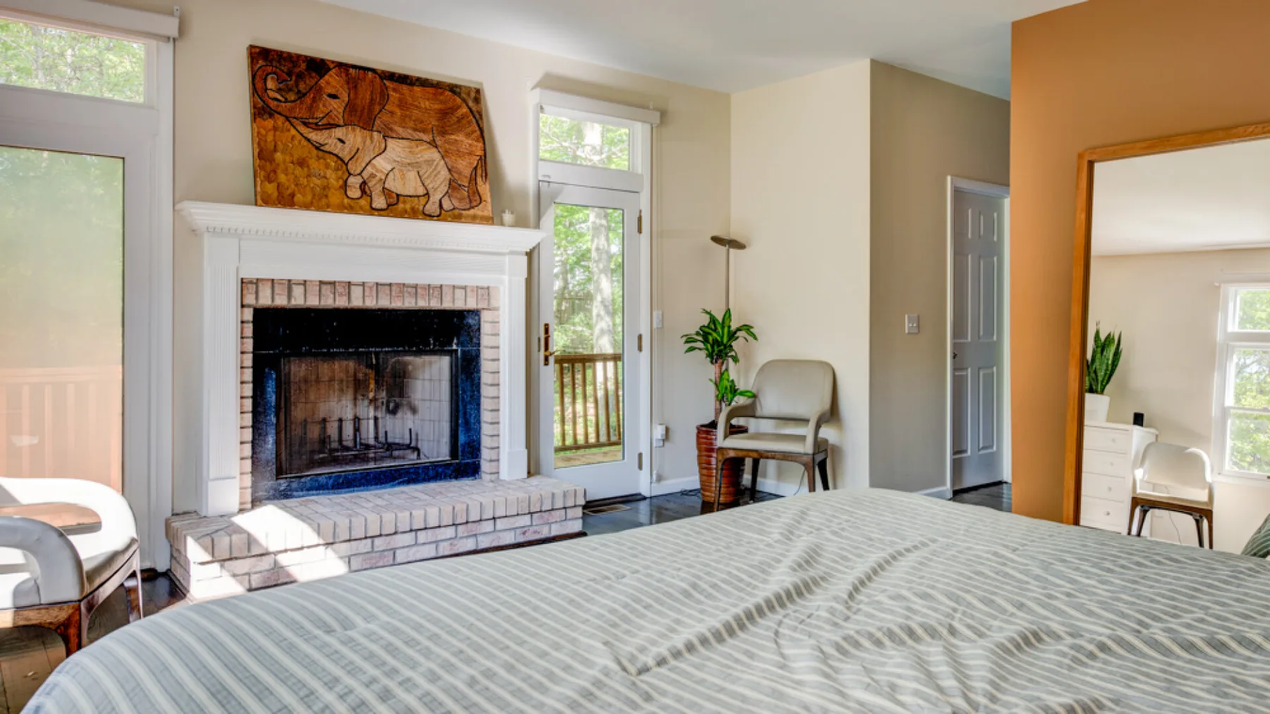 A bedroom with a large bed facing a fireplace and artwork above it.