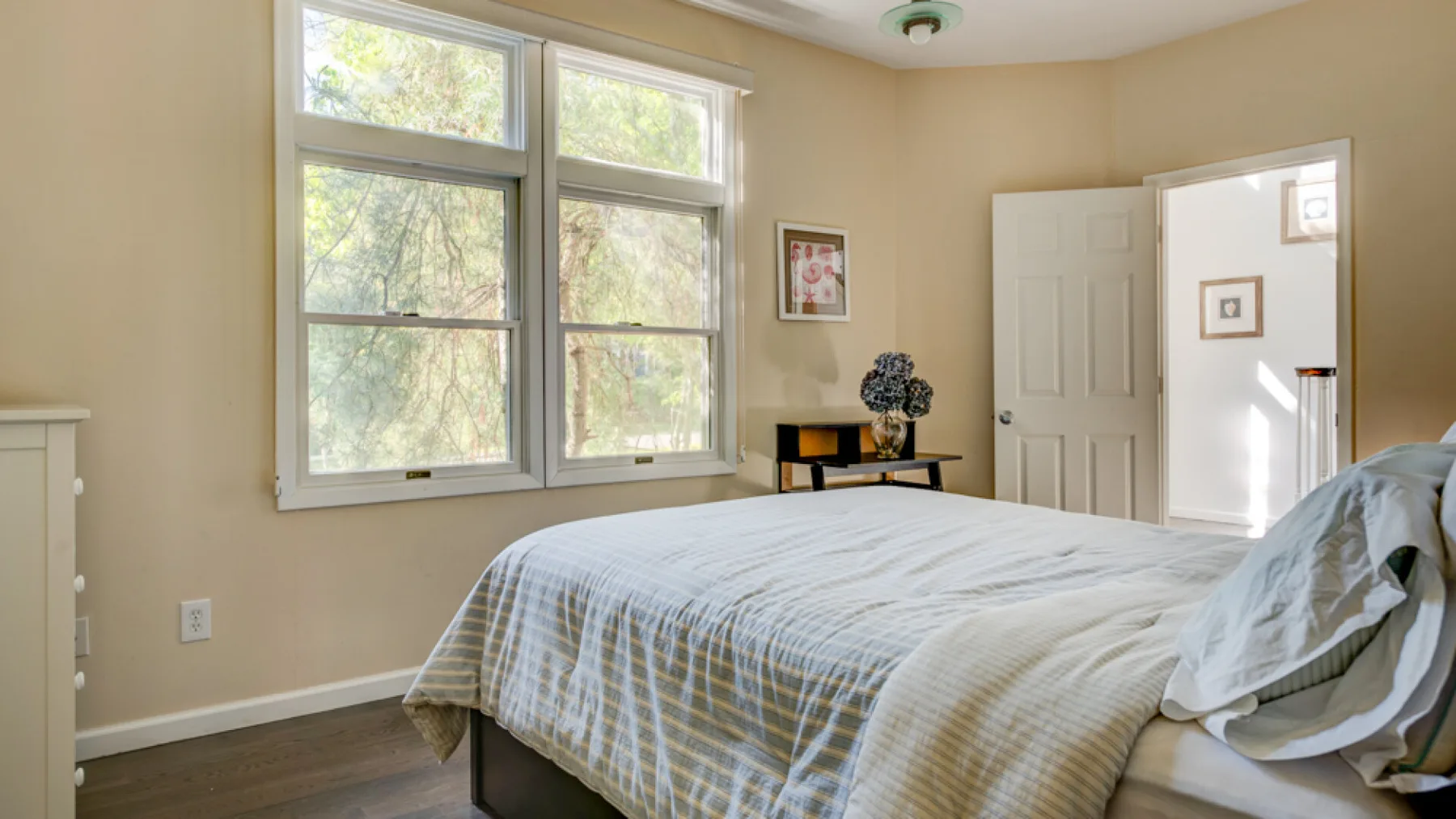 A bedroom with a bed beside two tall windows and an open doorway.