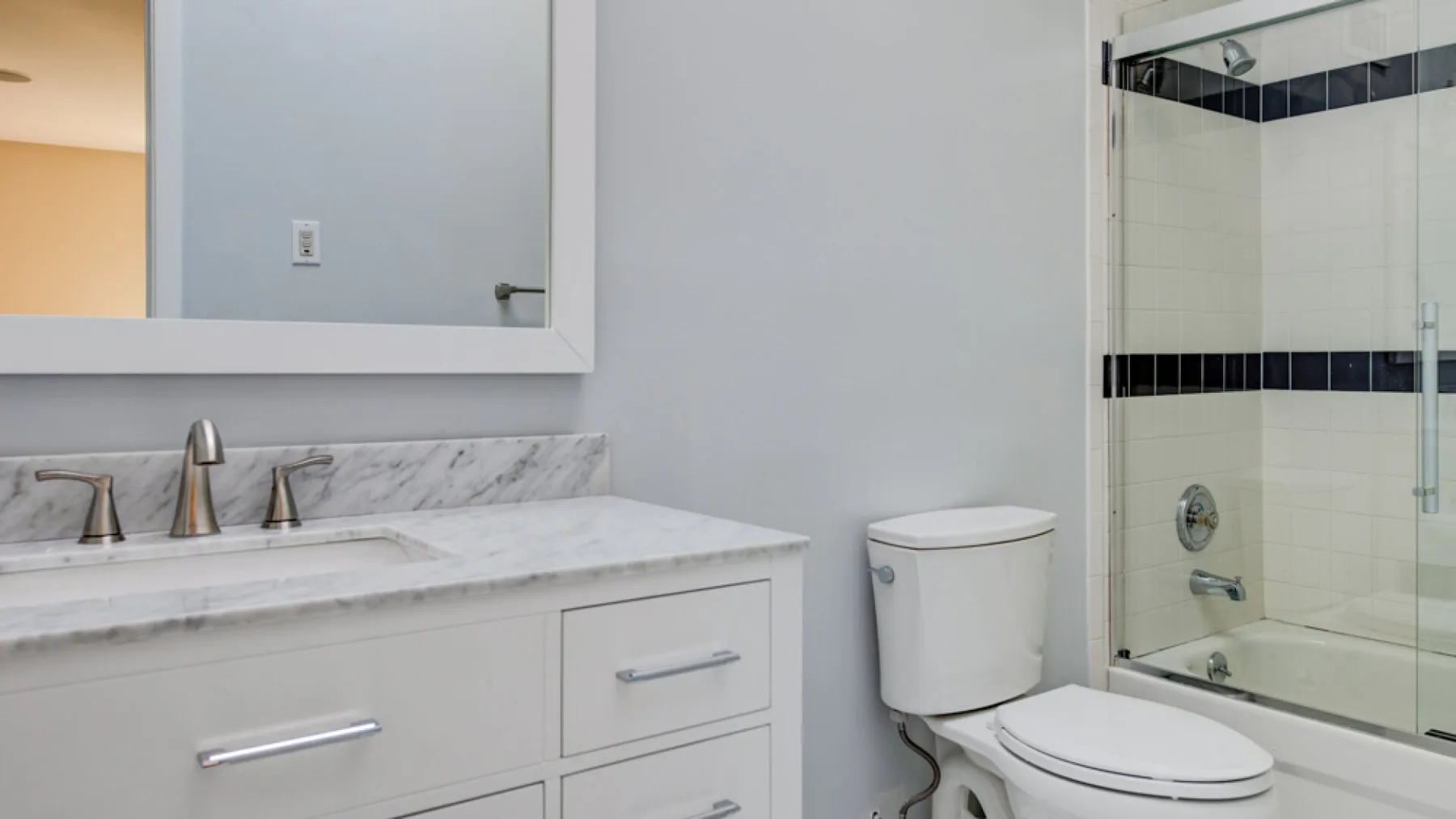 A bathroom vanity with a wide mirror sits beside a glass shower.