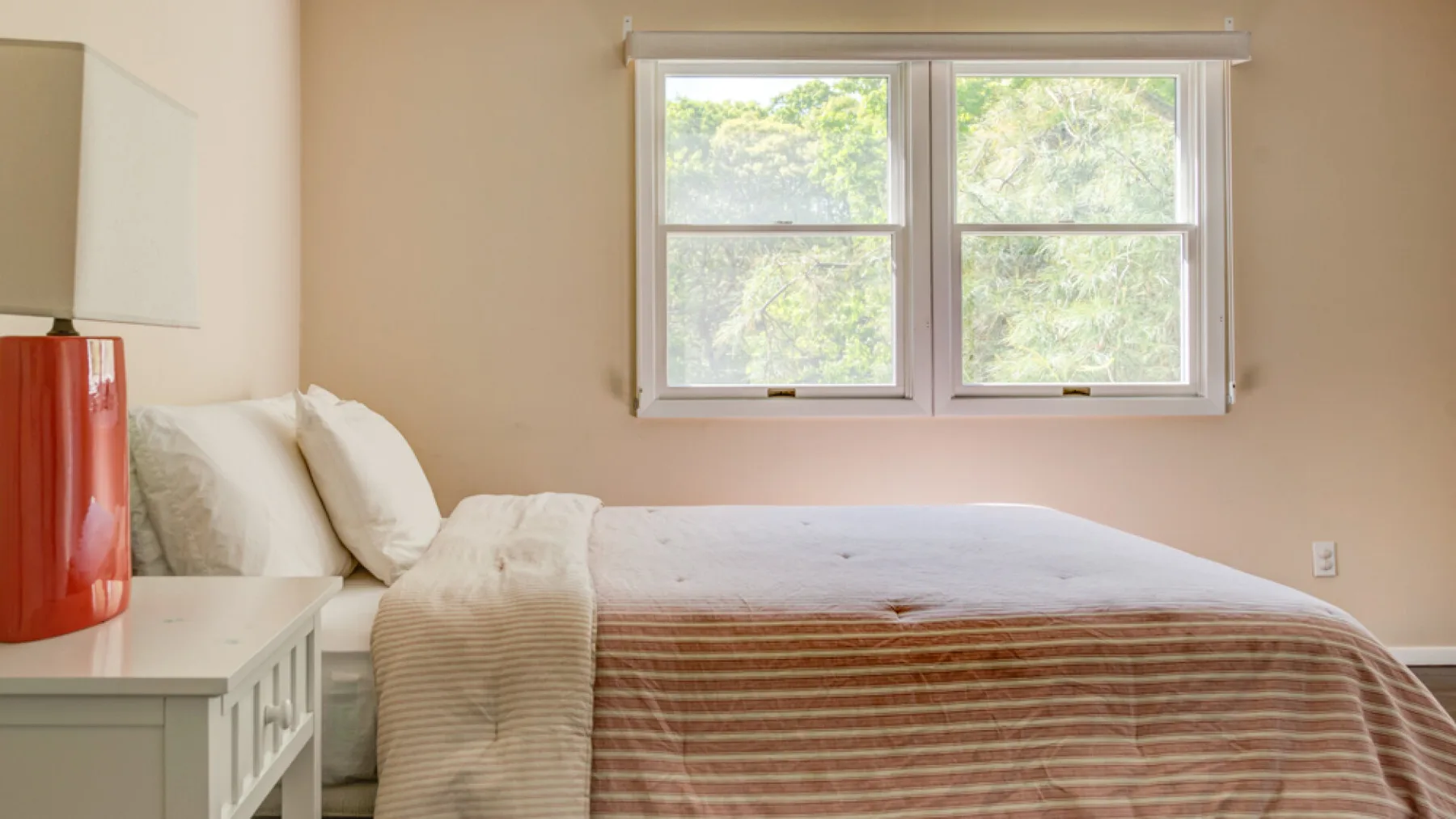 A bedroom with a bed beneath a window overlooking leafy trees.