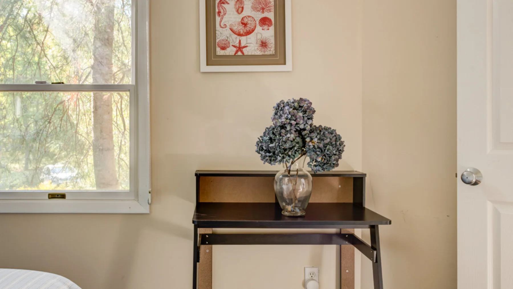 A small table with a vase of flowers stands beside a window.