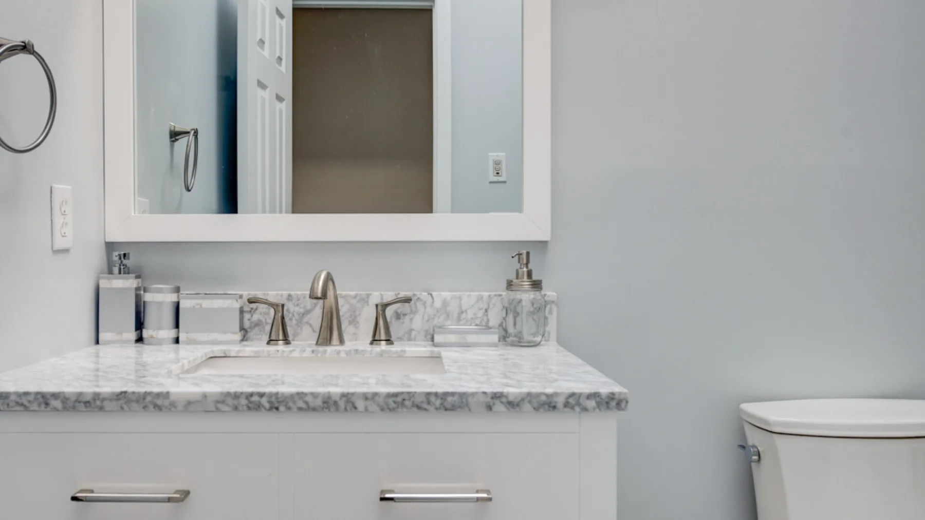 A bathroom vanity with a marble-patterned countertop and wide mirror.