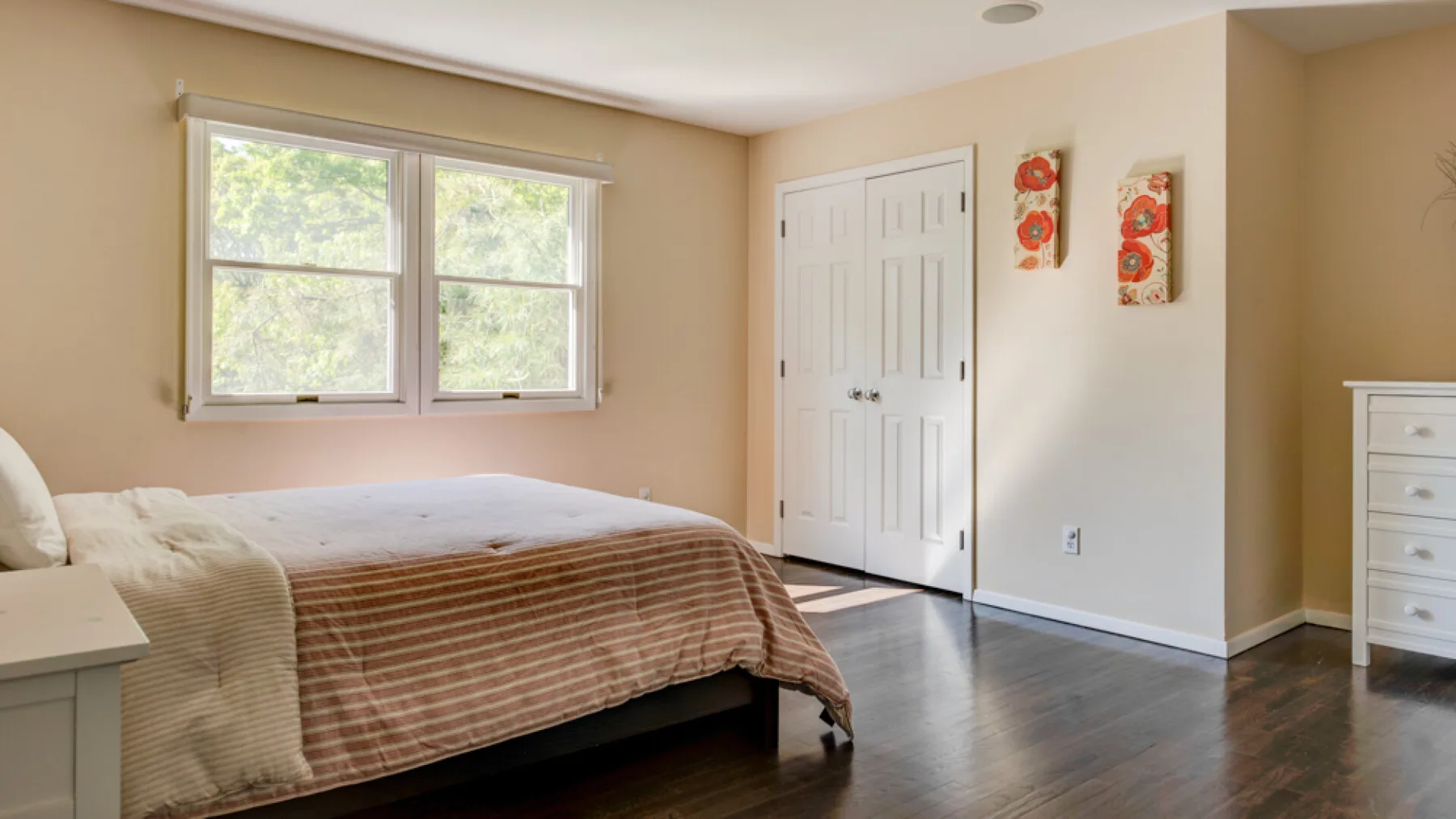 A bedroom with a bed beneath two windows and a pair of white doors.