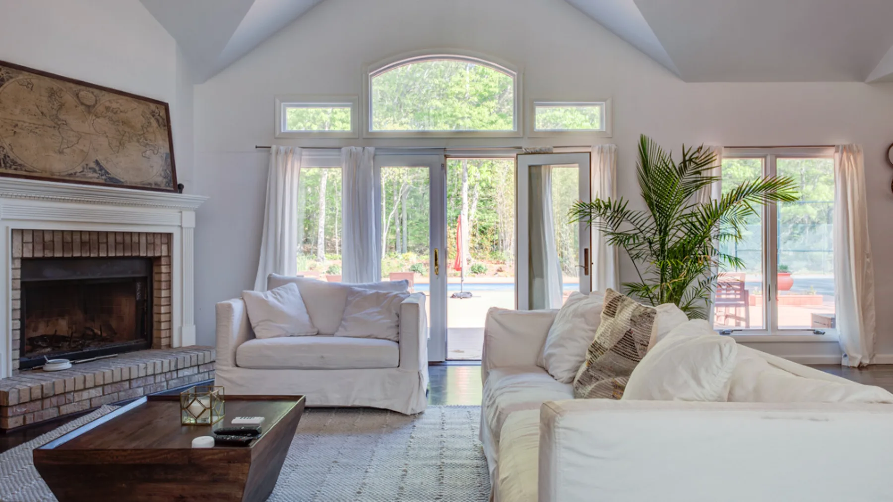 A bright living room with a fireplace, seating, and large windows overlooking greenery.