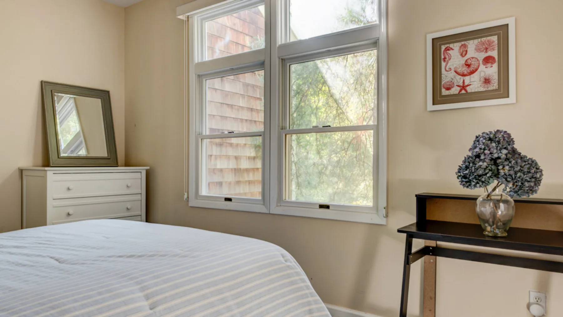 A bedroom with a bed, large windows, and a small table with flowers.
