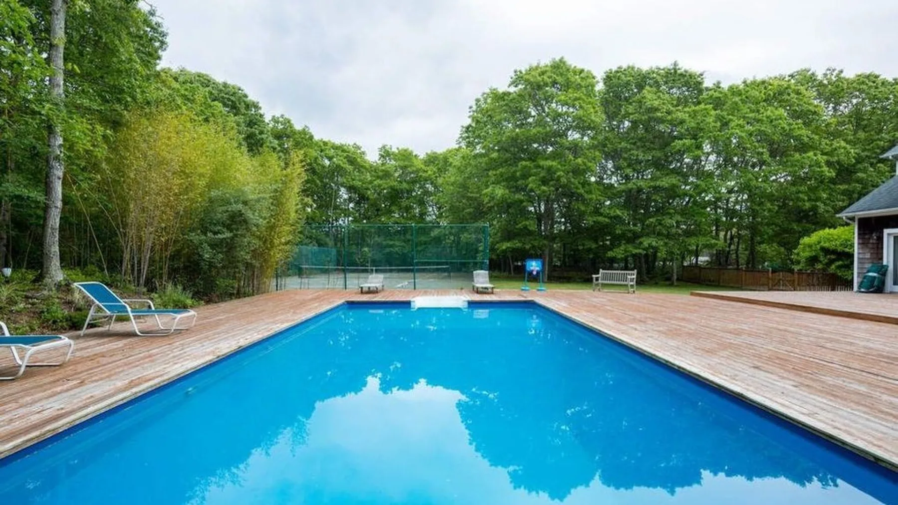 An outdoor swimming pool sits within a broad wooden deck, with trees surrounding the area.