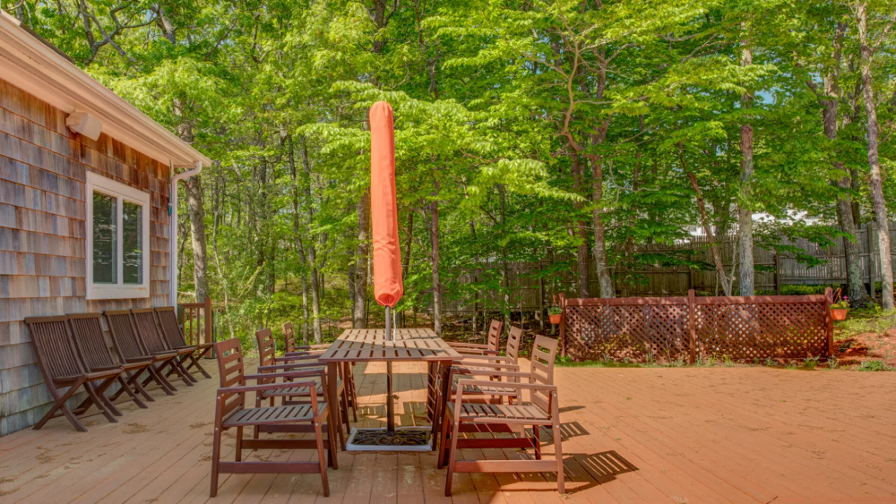 An outdoor patio with a wooden dining table and seating beneath leafy trees.