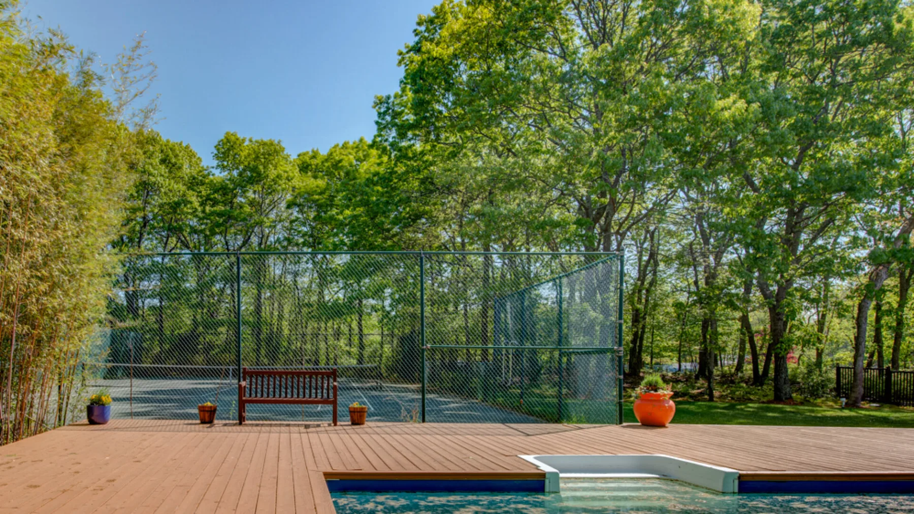 A fenced outdoor sports court sits beside a wooden deck and leafy trees.