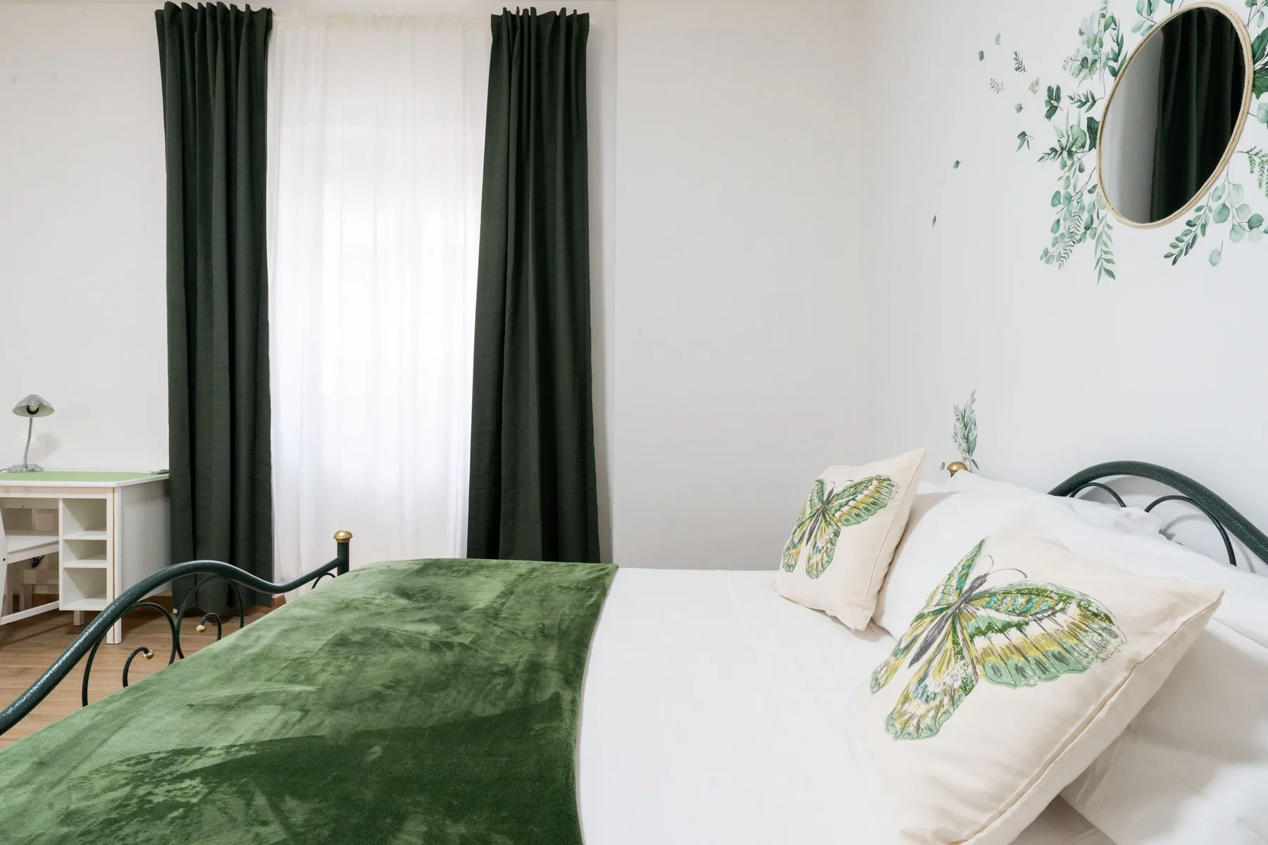 A bedroom with a bed dressed in green and white bedding beside a curtained window.