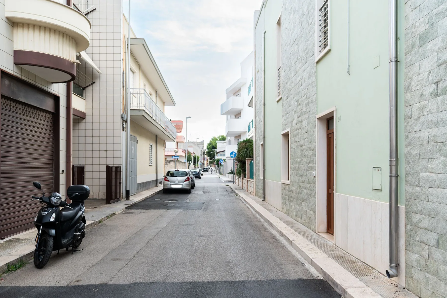 A narrow street runs between buildings, with parked vehicles along the road.