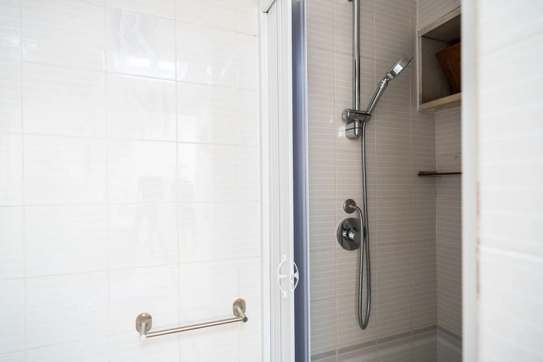 A tiled shower area with a handheld showerhead and wall-mounted controls.