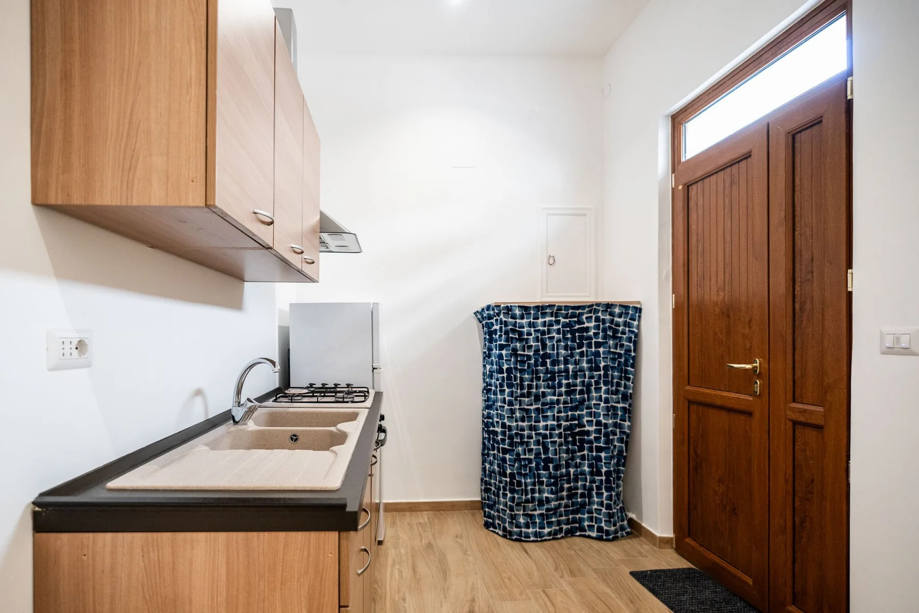 A compact kitchen with a sink and countertop beside a wooden door.