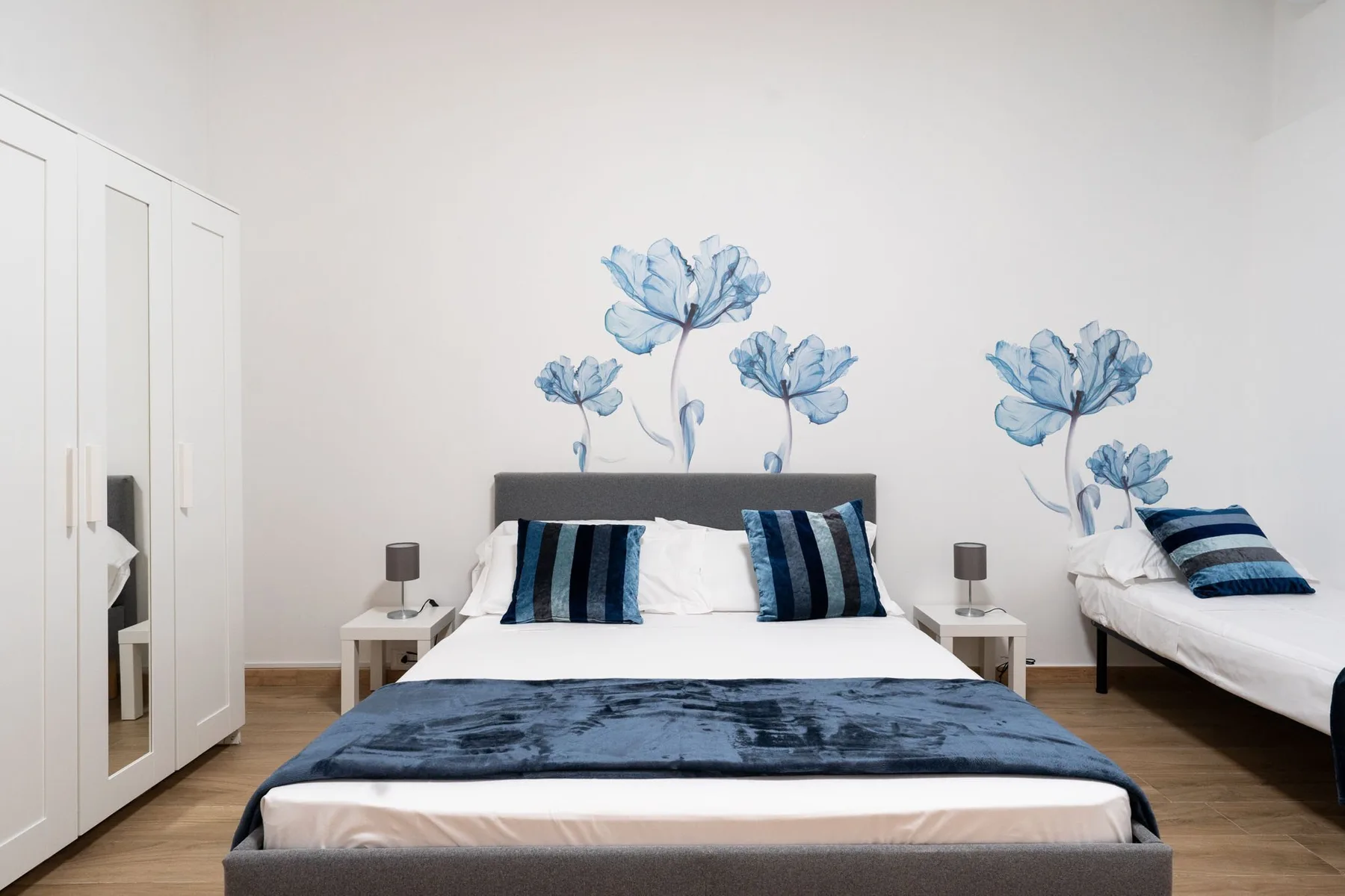 A bedroom with a large bed, blue bedding, and floral wall decorations.