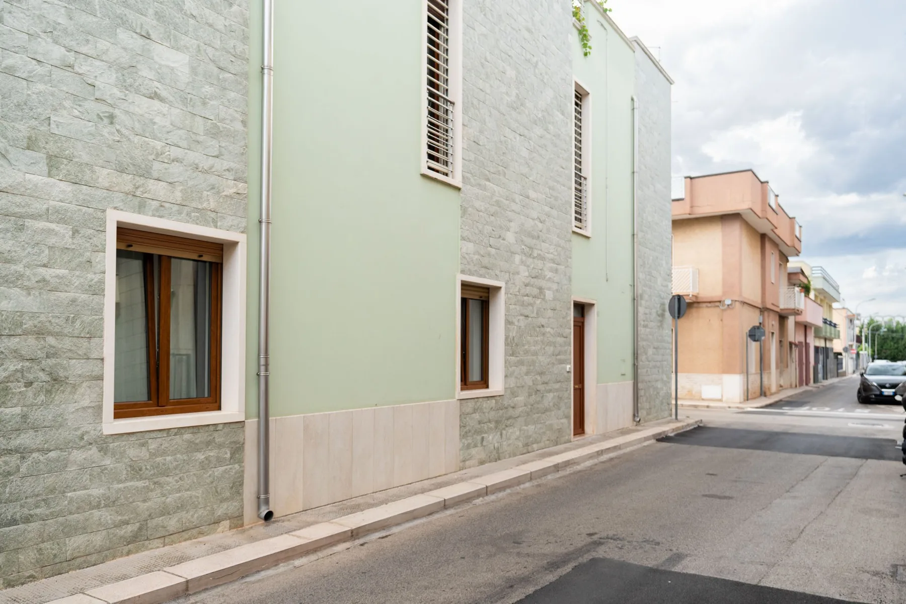 A quiet street lined with pastel buildings, including a pale green facade with stone cladding.