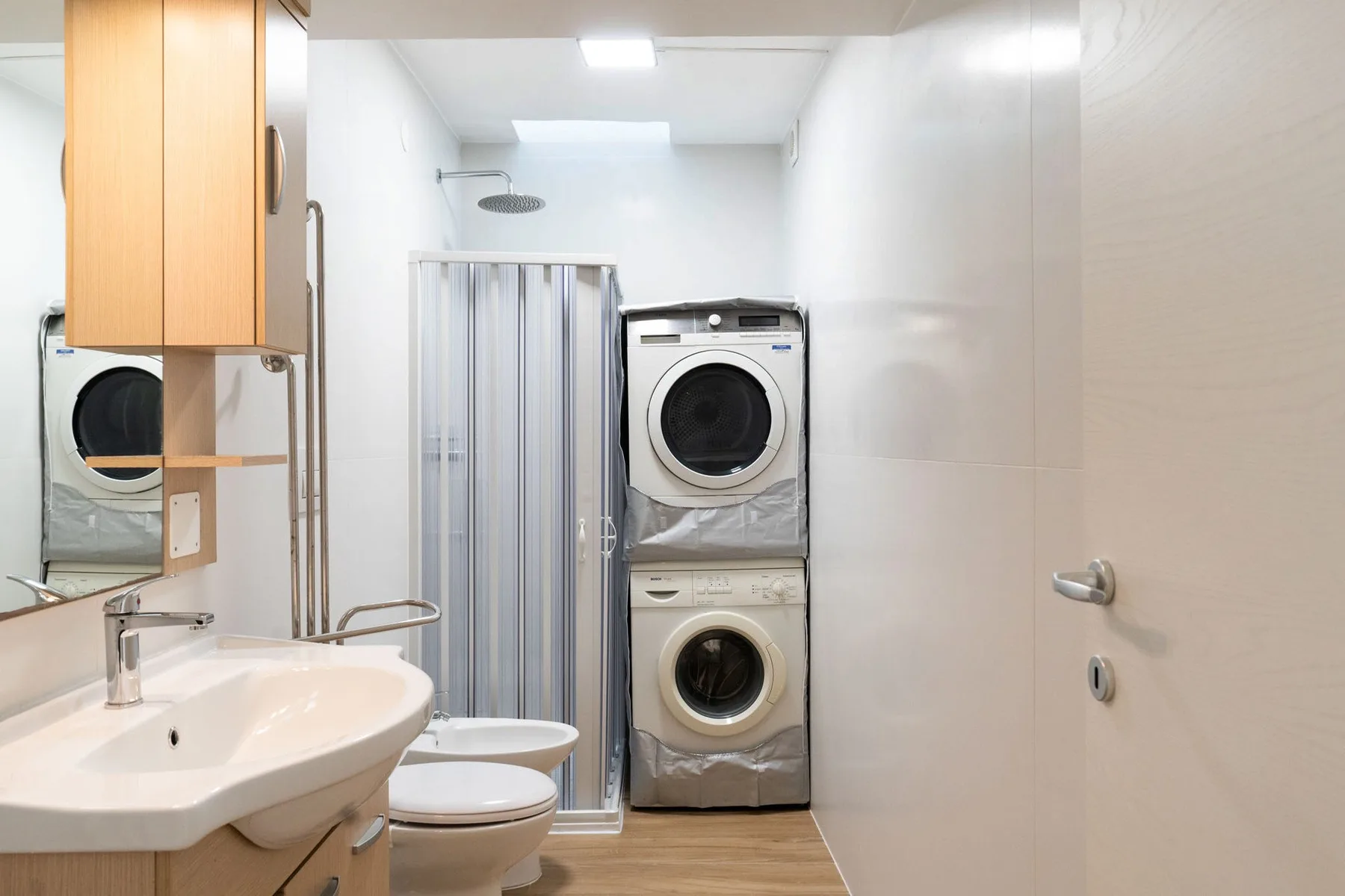 A bathroom with a shower, sink, toilet, and stacked laundry machines.
