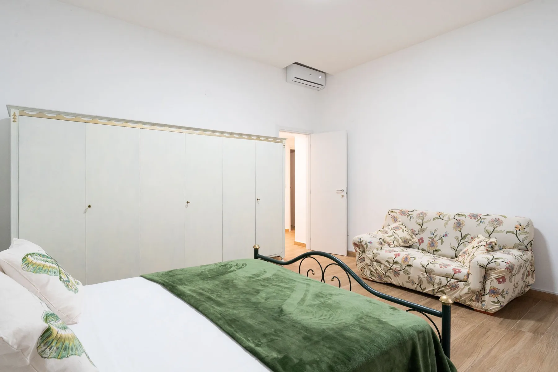 A bedroom with a bed covered by a green blanket and floral seating.