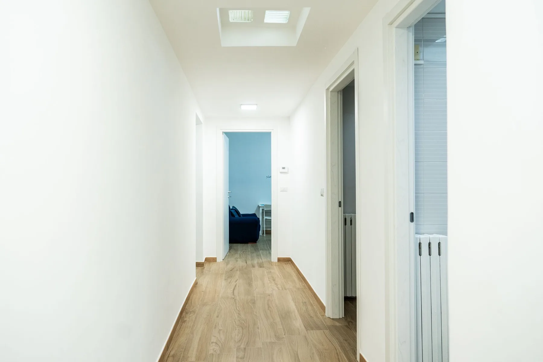 A bright interior hallway with wood flooring and several open doorways.