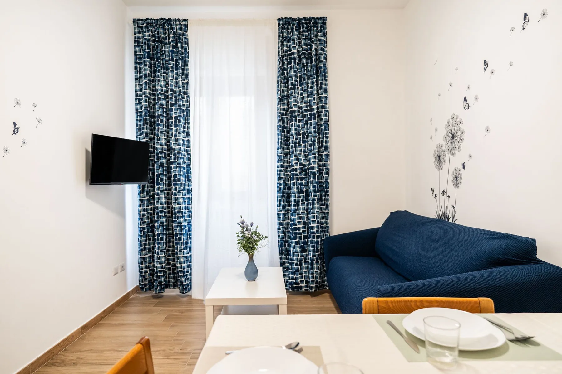 A living room with blue seating, patterned curtains, and a television.