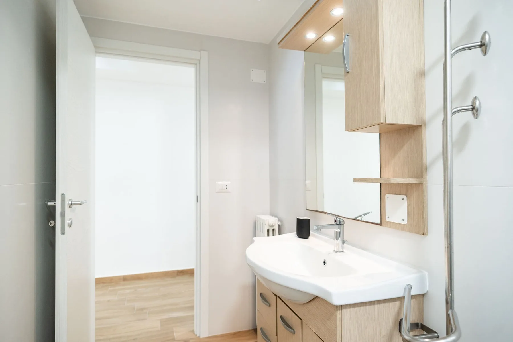 A bright bathroom with a sink, mirror, and open doorway.