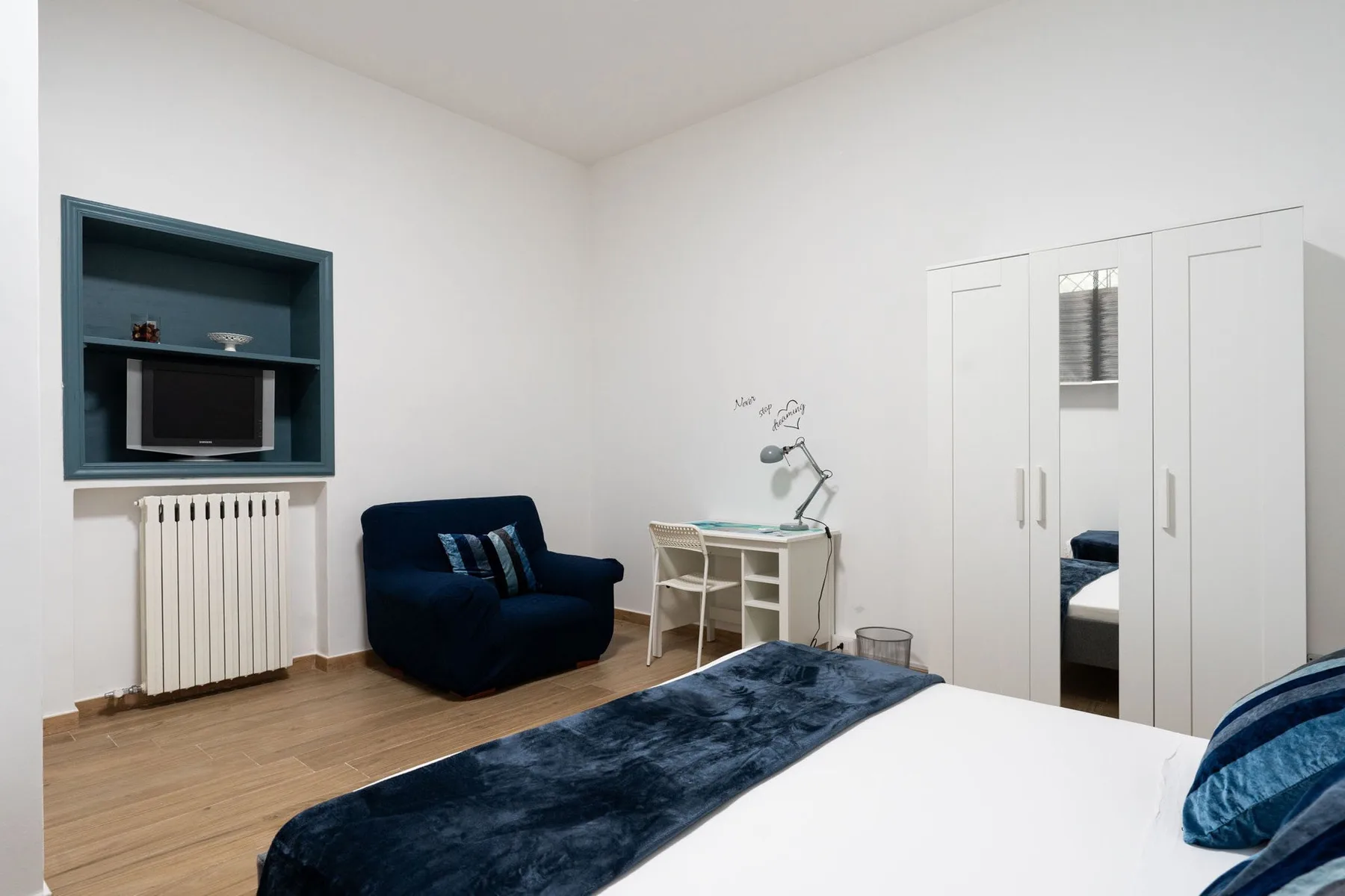 A bedroom with a bed, a desk, and a dark blue armchair.