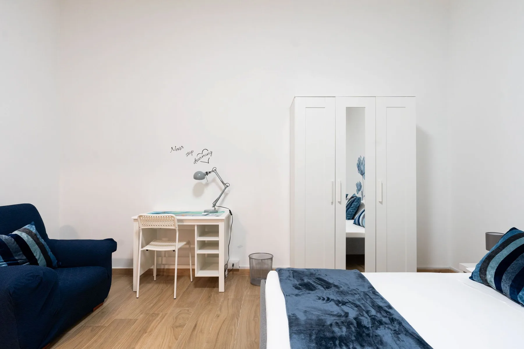 A bedroom with a desk, seating, and a bed with blue bedding.