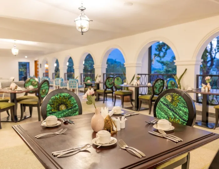 Una mesa de restaurante puesta con tazas, cubiertos y platos de acompañamiento, con la veranda con arcos extendiéndose al fondo.