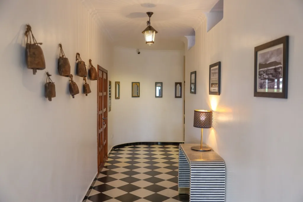 Un pasillo del hotel decorado con cencerros antiguos y fotografías de archivo enmarcadas, con un suelo ajedrezado en blanco y negro.
