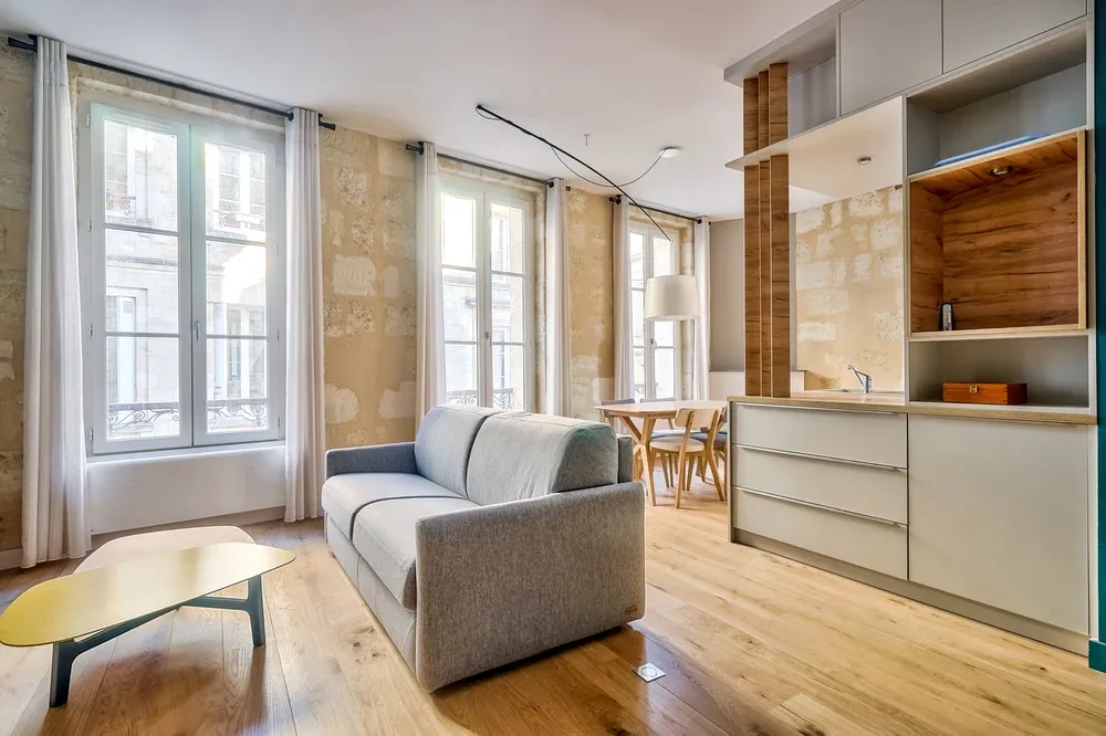 Una luminosa sala de estar con sofá gris, mesa de centro y ventanas altas.