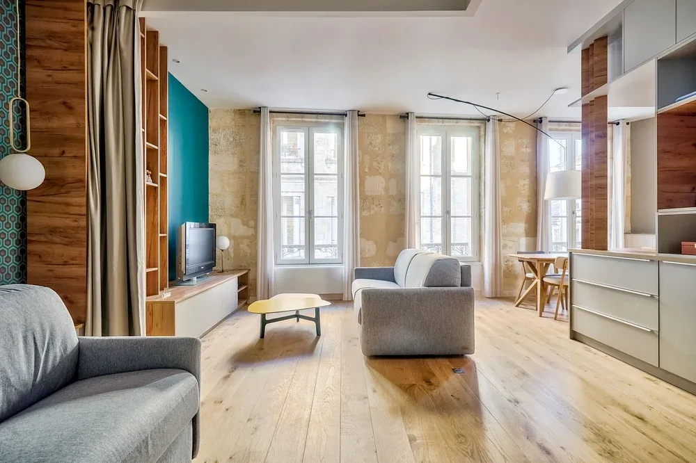 A bright living room with seating, a low table, and tall windows.