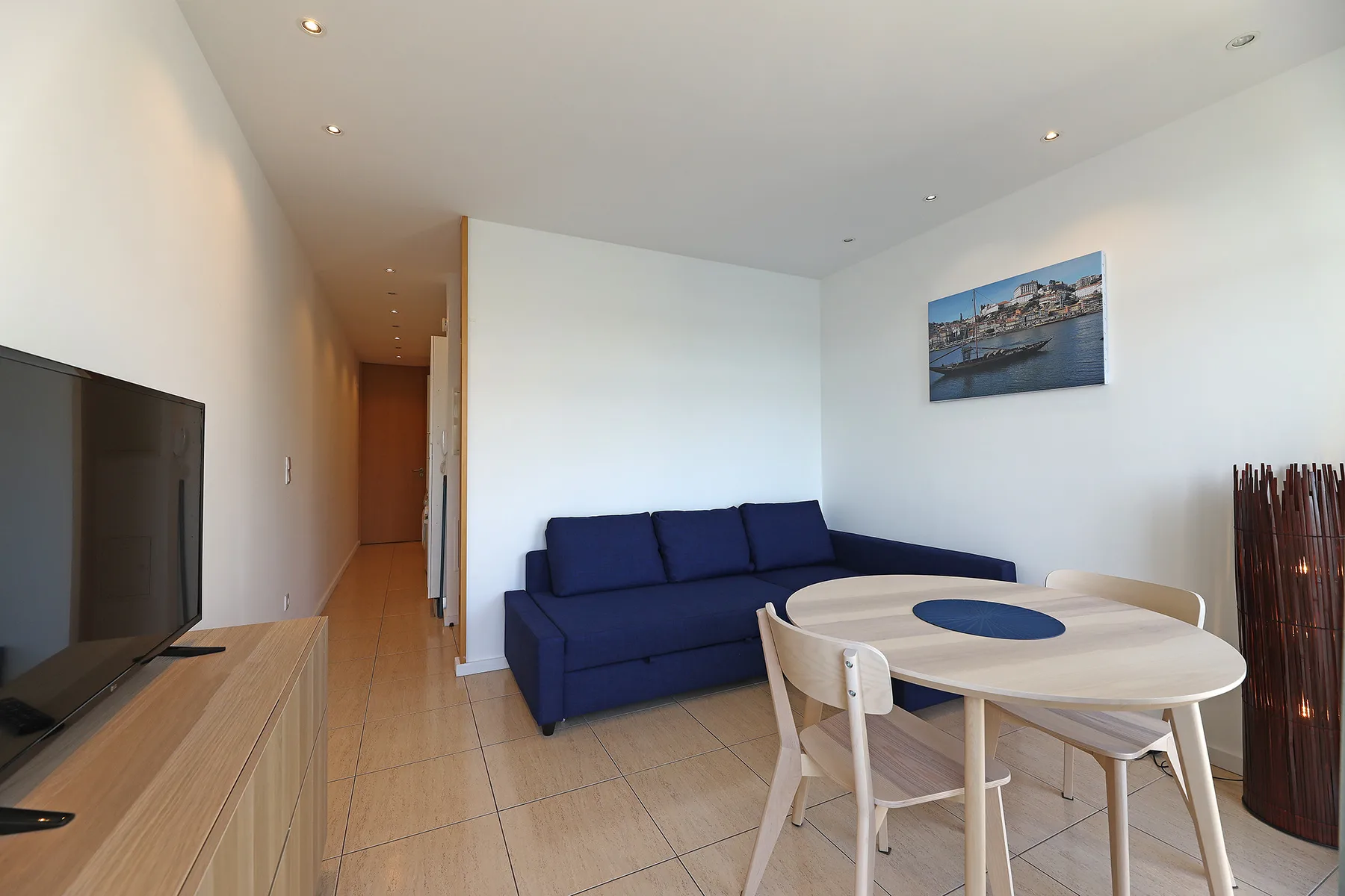 A bright living and dining area with blue seating, a round table, and a television.